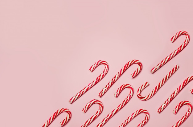 Pattern of striped candies in Christmas colors on baby pink background. Red and white striped hard candy cane