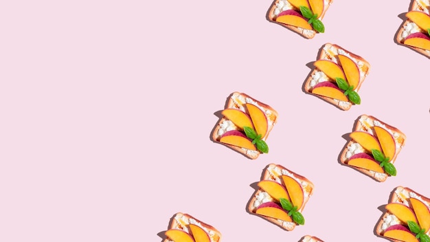 Pattern of toasted bread with peach and basil on pink background