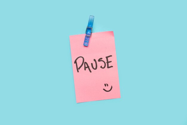 Pause word written on a pink sticky paper on a blue background