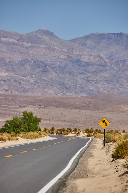 Paved road in desert landscape leading to sharp turn and mountains