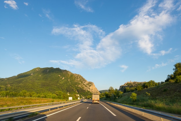 Paved two lane road in scenic alpine landscape and moody sky. Panoramic view from car mounted camera.