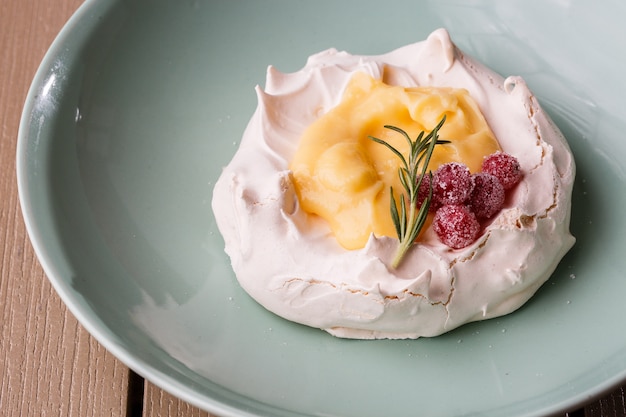 Pavlova mini cake with custard cream and fresh summer berries on green plate on wooden