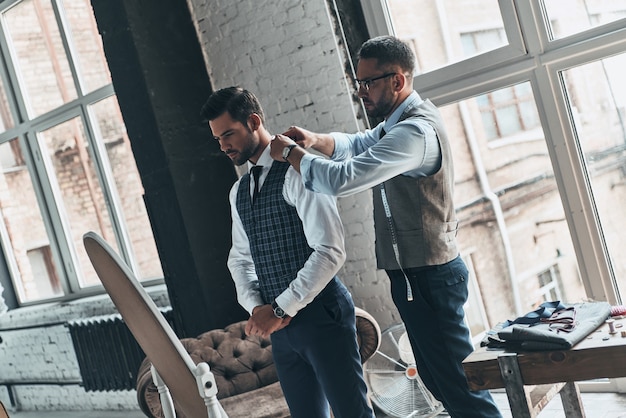 Paying attention to every detail. Young fashionable designer helping his client to get dressed 