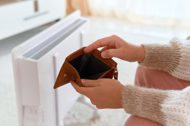 Payment of bills Cold winter and rising prices for heating natural gas and electricity Crisis concept Female hands hold empty wallet near the radiator