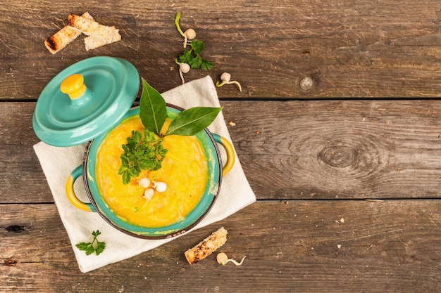 Pea cream soup in a bowl on vintage wooden background Dry legumes toast croutons and greens