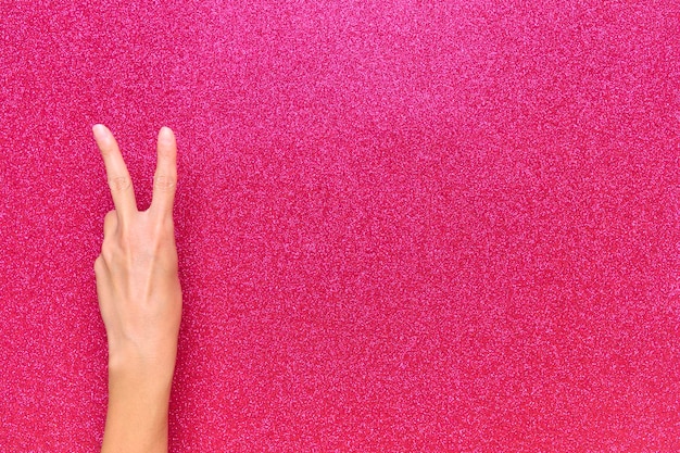 Peace gesture in woman hand on bright pink background with copy space