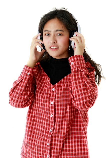 Peaceful Asian female in cool outfit listening to music in headphones on white background in studio.