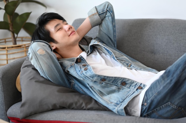 Peaceful asian man relaxing on comfortable sofa at home