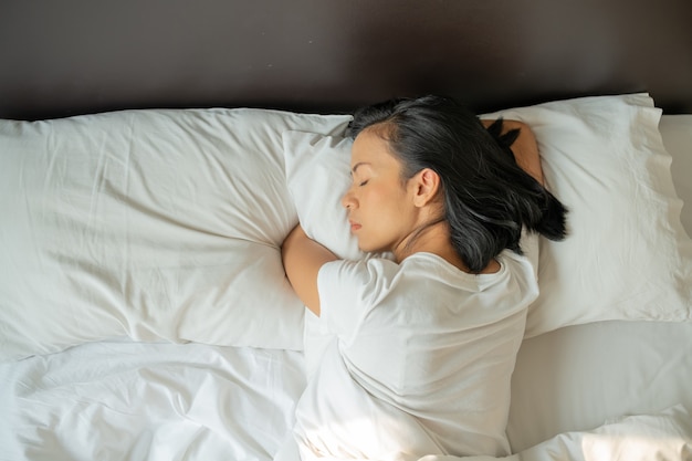 Peaceful serene young lady wear pajamas lying asleep on the bed. Top view