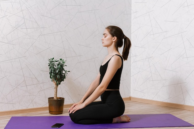 Peaceful woman with closed eyes sitting on mat in Hero pose and meditating