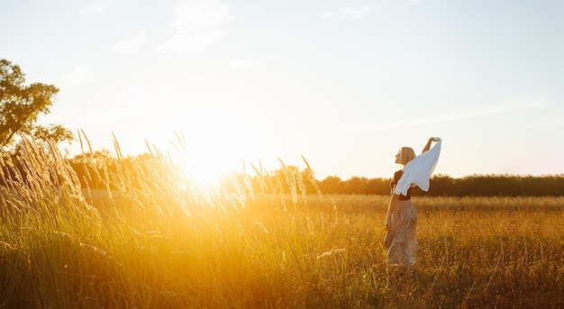 Peaceful young blond woman standing amidst wheat field Against setting sun