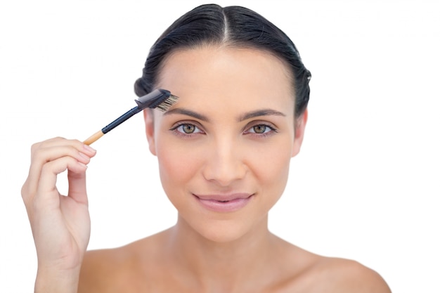 Peaceful young brunette using eyebrow brush