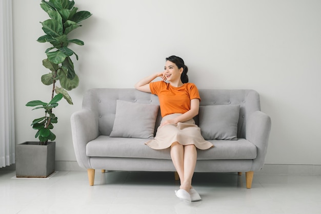 Peaceful young woman with hands behind head relaxing on cozy sofa at home