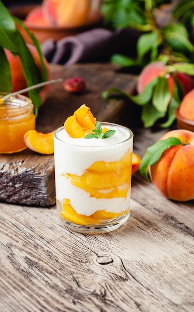 Peach fruit dessert in glass cup on wooden table. Fruit salad with yogurt or sour cream.