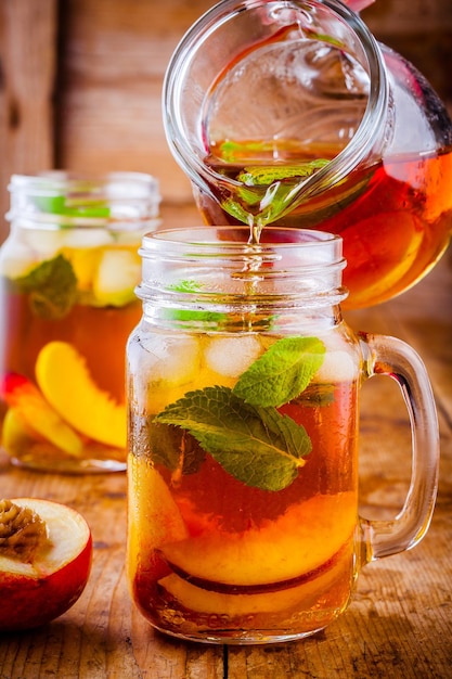 Peach ice tea in mason jar with mint on wooden table