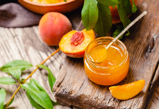 Peach jam in glass jar with peach wedges and whole fruit. Peach jam on wooden table. Canned fruit jam with ingredients.