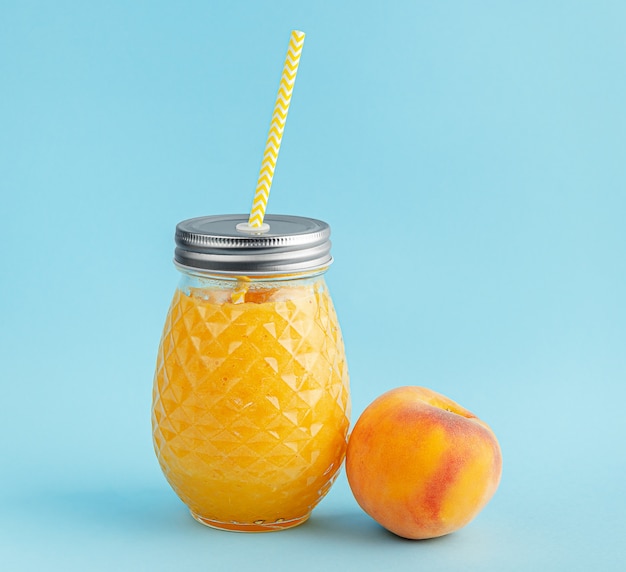 Peach smoothie jar with yellow drinking straw on blue wall.