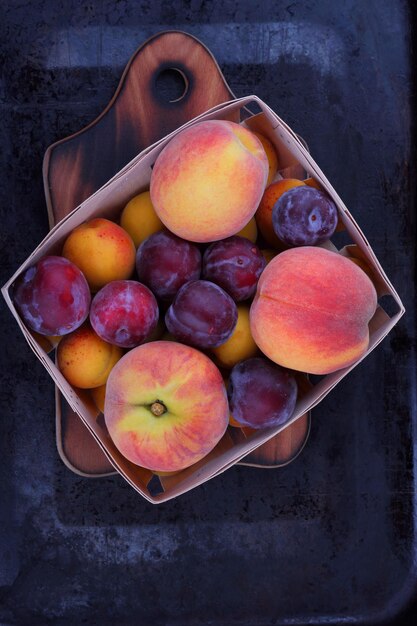 Photo peaches apricots and plums in a wooden basket on a wooden board on a dark background beautiful composition of juicy fruits closeup