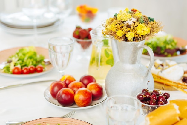 Peaches and sweet cherries lying on plates near vase with flowers