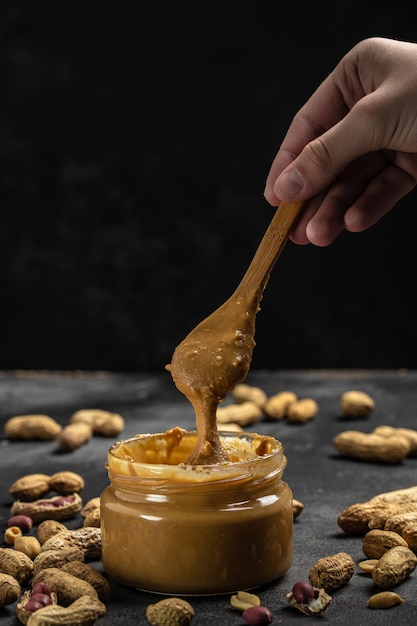 Peanut butter in glass jar and spoon on dark background American dessert concept vertical image top view place for text