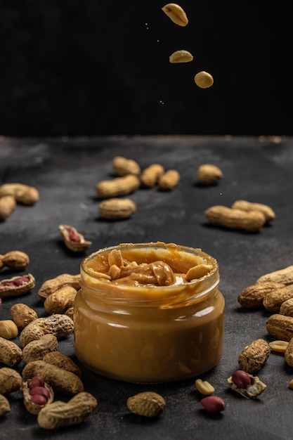 Peanut butter in glass jar and spoon on dark background American dessert concept vertical image top view place for text