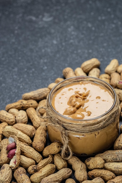 Peanut butter in glass jar and spoon on gray background American dessert concept vertical image top view place for text