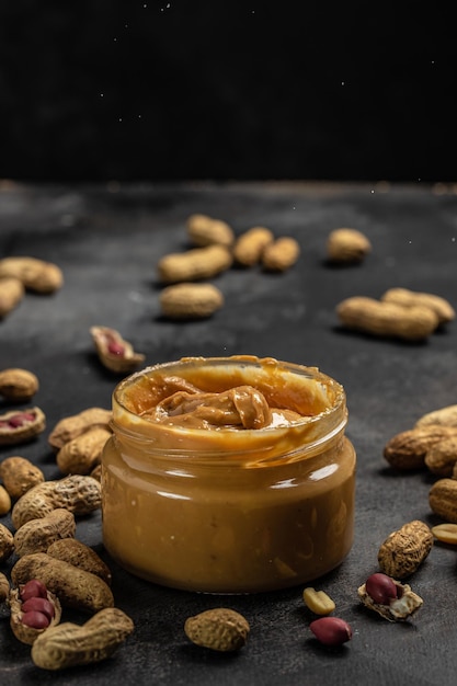 Peanut butter in glass jar and spoon on gray background American dessert concept vertical image top view place for text