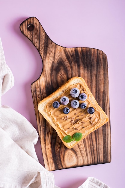 Peanut butter toast with blueberries flax seeds and mint on a cutting board Top and vertical view