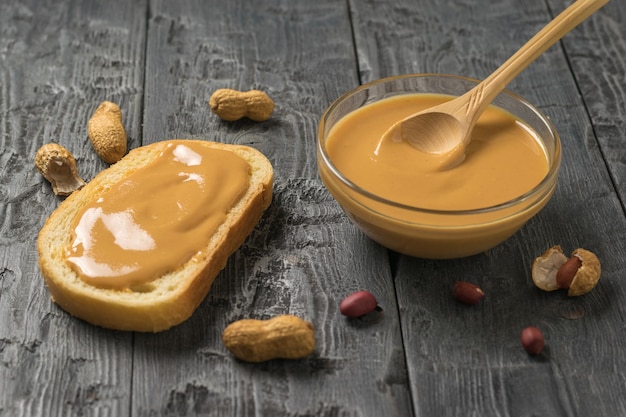 Peanut paste in a bowl and on a piece of bread on a wooden table