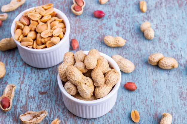 Peanuts in a white bowl rests on an old wooden table.