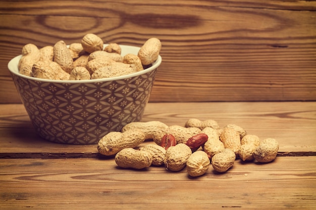 Peanuts with shell in a bowl and on a wooden table