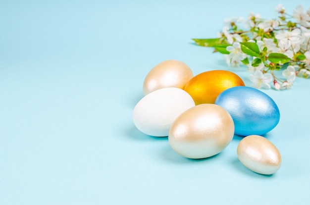 Pearl colored eggs for Easter with branches of blossoming cherry on blue