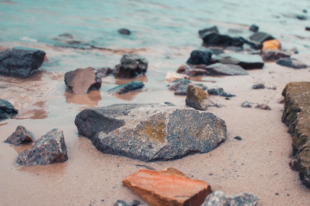 Pebbles on a sandy shore in clear water. The silky waves of a blue lake hit the stones. Natural background.