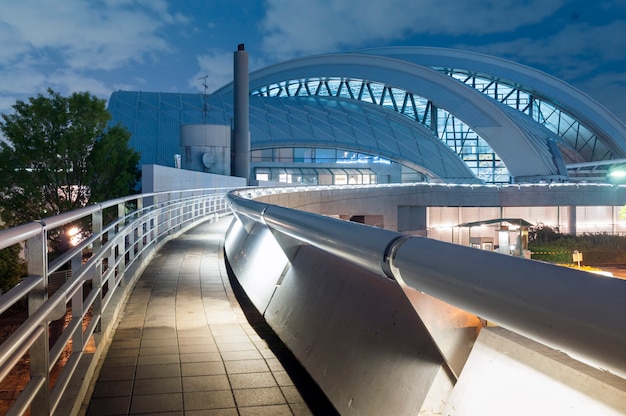 Pedestrian pathway with metallic handrail leads toward modern arc dome building by night