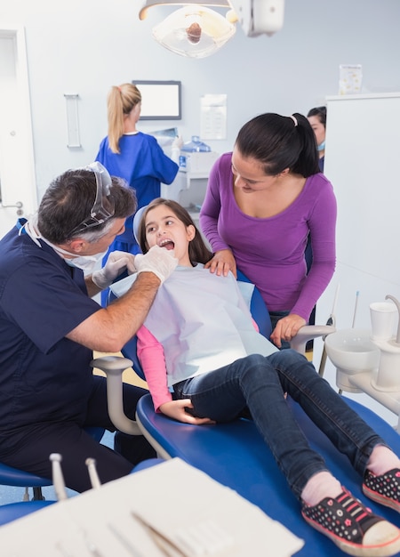 Pediatric dentist examining young patient with her mother