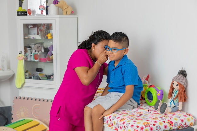 Pediatric doctor checking the ear of a child who is sitting on the bed in the office