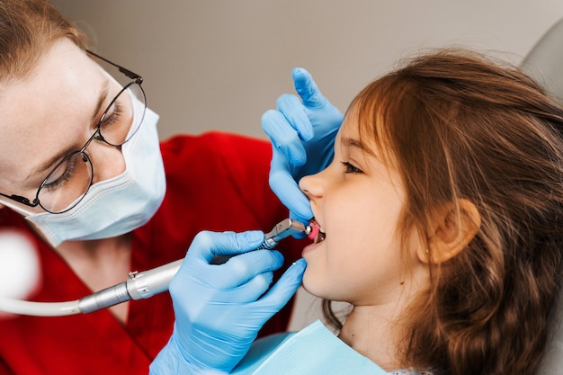 Pediatric girl dentist makes professional teeth cleaning in dentistry Professional hygiene for teeth of child in dentistry Pediatric dentist examines and consults kid patient in dentistry