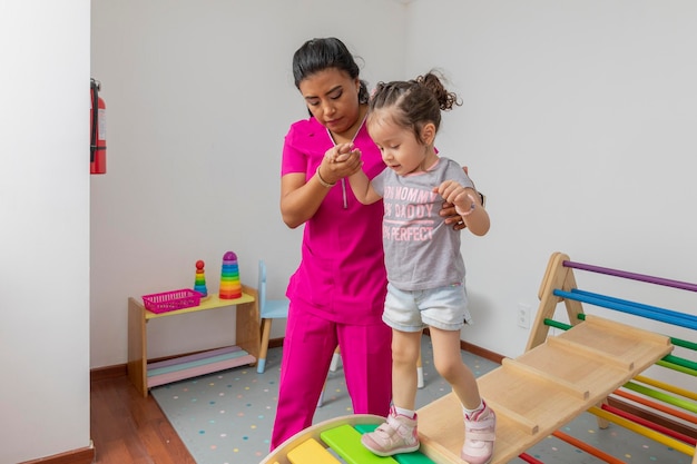 Pediatric nurse helping a girl walk through a wooden game in her medical office