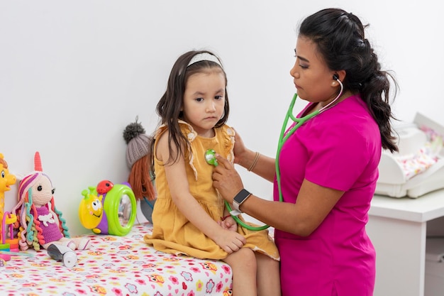 Pediatrician doctor checking with the stethoscope a little girl sitting on a stretcher