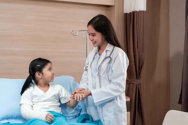 Pediatrician doctor examining little asian girl with a broken arm wearing a cast at hospital