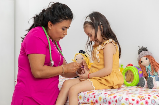 Pediatrician doctor placing a bandaid on the finger of a girl in a yellow dress sitting on the couch in the office