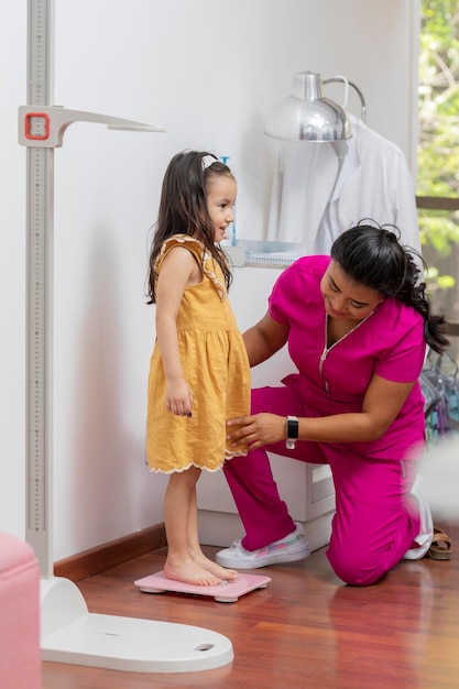 Pediatrician doctor weighing a girl on a floor scale in her office