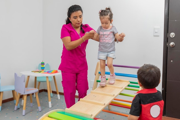 Pediatrician helping a girl to walk through a wooden game while a boy watches them