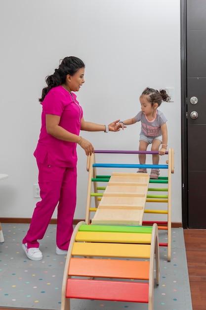 Pediatrician helps a girl to climb on a wooden game that he has in his office