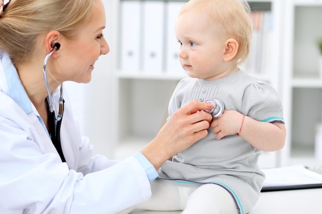 Pediatrician is taking care of baby in hospital. Little girl is being examine by doctor with stethoscope. Health care, insurance and help concept.