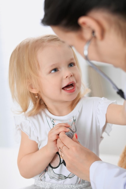 Pediatrician is taking care of baby in hospital. Little girl is being examine by doctor with stethoscope. Health care, insurance and help concept.