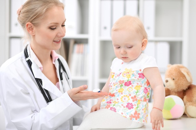 Pediatrician is taking care of baby in hospital. Little girl is being examine by doctor with stethoscope. Health care, insurance and help concept.