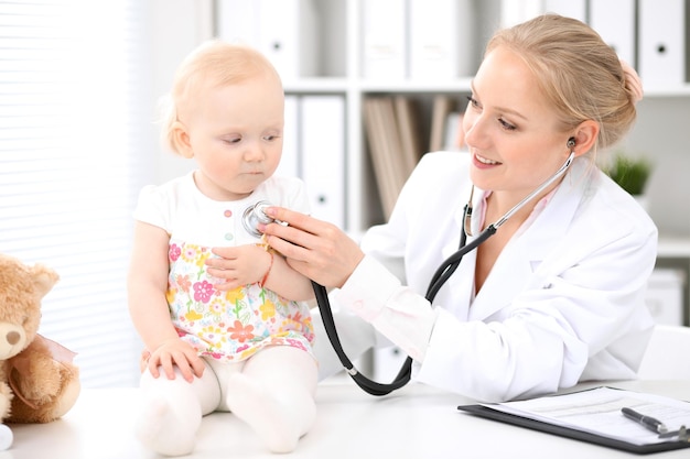 Pediatrician is taking care of baby in hospital. Little girl is being examine by doctor with stethoscope. Health care, insurance and help concept.