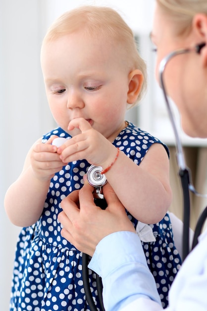 Pediatrician is taking care of baby in hospital. Little girl is being examine by doctor with stethoscope. Health care, insurance and help concept.