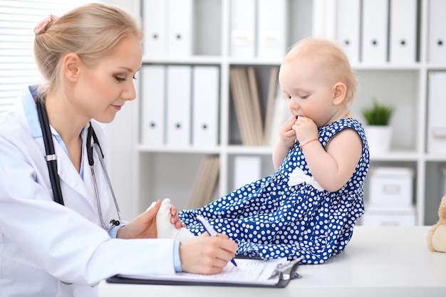 Pediatrician is taking care of baby in hospital. Little girl is being examine by doctor with stethoscope. Health care, insurance and help concept.